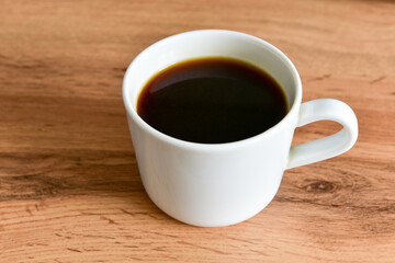White cup of strong black coffee on wooden surface close up