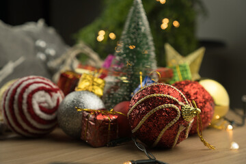 Wooden table with Christmas decorations. Red, silver and gold balls, gift boxes, lights, Christmas tree and others. Selective focus.
