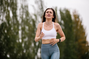 Fototapeta premium Woman running, wearing sports clothes. With an effort expression. With a park in the background. Women, fitness and sport concept