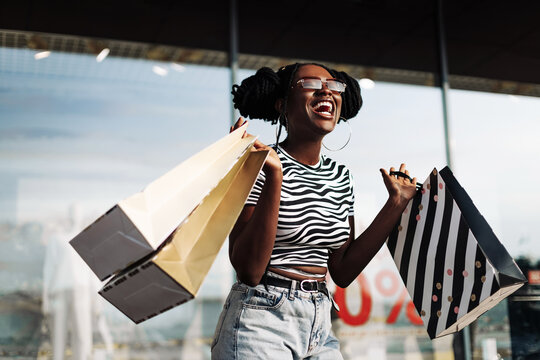 African American woman, wearing sunglasses, standing in a mall with shopping bags in her hands