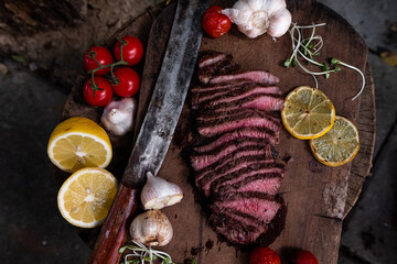Roast beef on cutting board with saltcellar Garlic,tomatoes and lemon