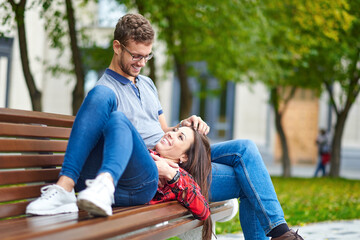 Lovely portrait of a young couple. They are sitting on the bench, embracing and kissing.
