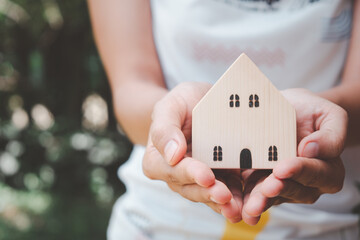 Woman hand holding wooden house with copy space, homeless housing and home protecting insurance concept, international day of families, homeschooling, Top view.