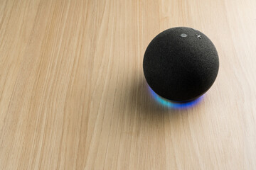 Smart speaker and a virtual assistant. It is used to keep the home connected and give orders by voice to other electronic devices. Modern technology. Wooden background.