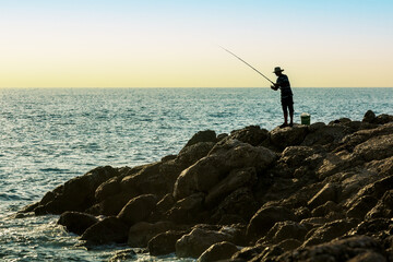 Fishing man silhouette at sunset. People enjoying weekend hobby in holidays.