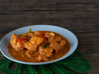 Ayam Kapitan (Kapitan Chicken), Malaysian Curry close up on dark background with copy space. Spicy Asian curry with coconut gravy and chili on wooden table.