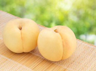 Fresh Yellow Peach over blurred greenery background, Yellow Peach Peach fruits on bamboo mat.