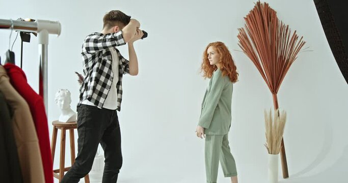 The process of advertising shooting stylish clothes red-haired girl with curly hair model posing in front of the camera photographer takes pictures in a stylish photo studio backstage