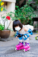 Little girl wearing a white face mask is learning how to balance on a pink inline skate on the...