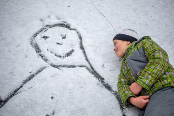 happy boy lies in the snow near the drawn picture