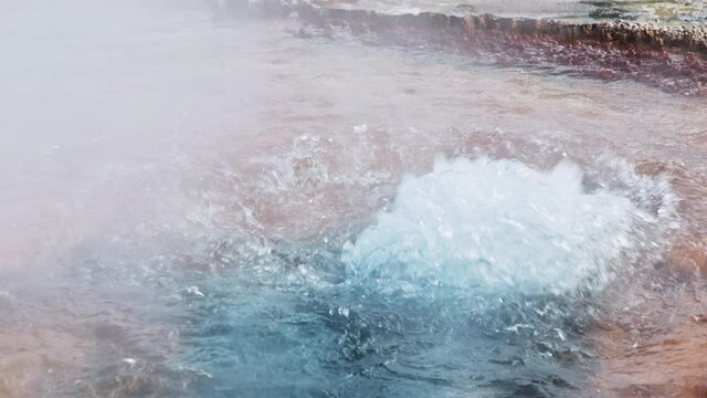 Scenic slow motion of active hot geyser in Yellowstone National park volcano. Geothermal hot spring with boiling water in sulfur, smoking fumaroles and blue orange colors. Erupting volcano geyser 4K