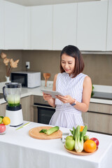 Obraz na płótnie Canvas Asian woman using tablet to find recipe making smoothie with fruit and vegetable in kitchen.