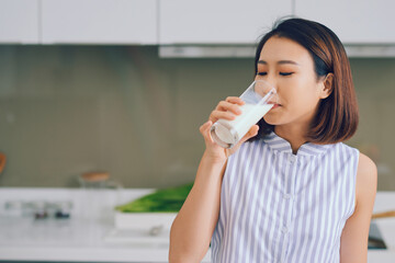 Portrait of young Asian woman drinking milk while standing in the kitchen.