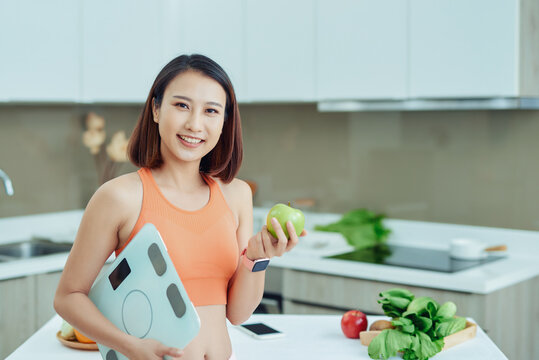 Asian woman holding apple and scale in the kitchen