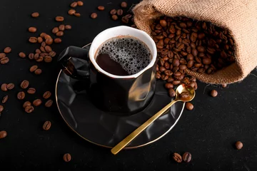 Keuken foto achterwand Koffie Una taza de café negro con una cucharita dorada al costado, y granos de café esparcido  