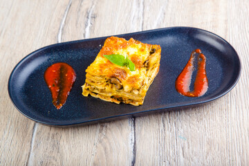 italian lasagna with tomato sauce on a black plate and wood background top view