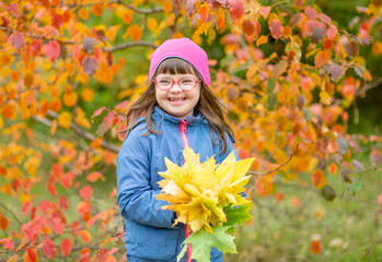 Laughing young girl with down syndrome holding bouquet of autumn leaves