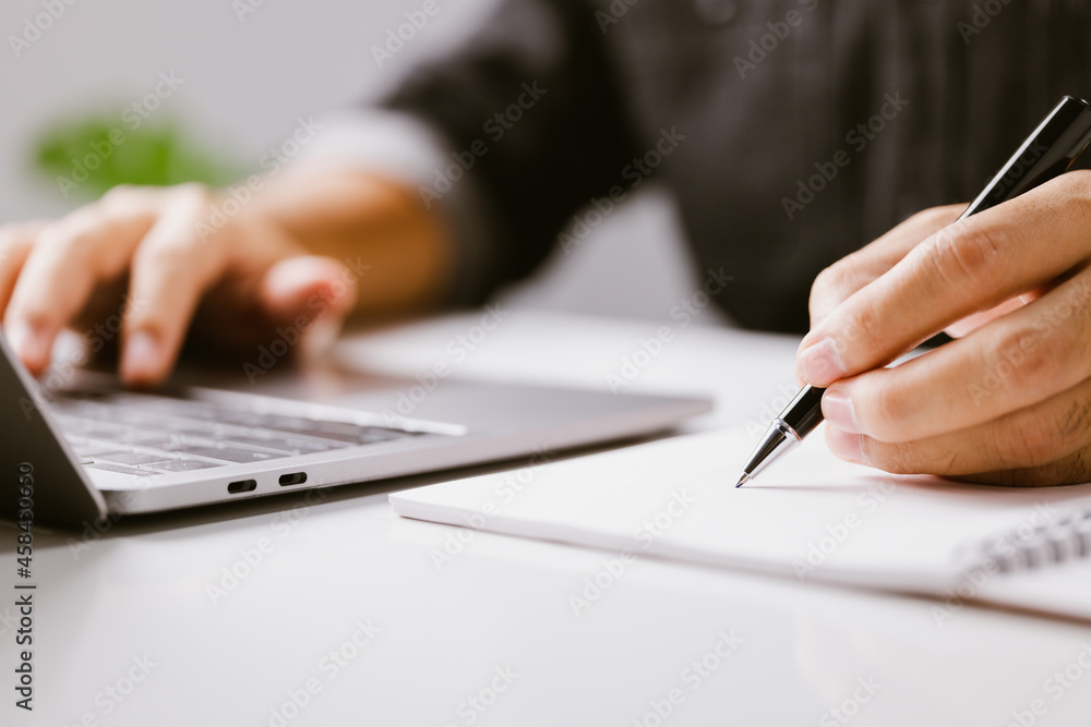 Poster closeup hand of business man writing on note while using laptop computer on desk at home, male plann