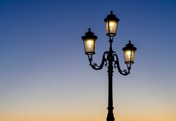 Fototapeta na wymiar Street lamp lit in the blue sunset sky
