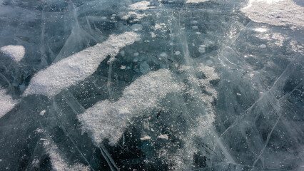 Turquoise transparent ice of a frozen lake. Close-up. Full-screen mode. Deep intersecting cracks,...