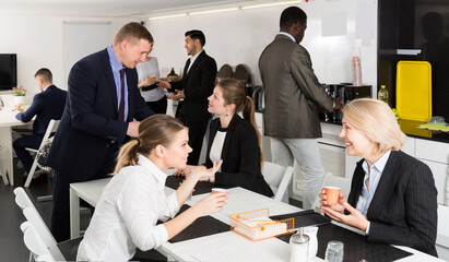 Cheerful multinational colleagues having break at office, drinking coffee and talking