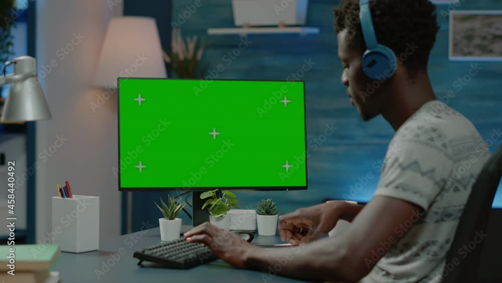 Poster African american man working with horizontal green screen on computer monitor. Black person with headphones looking at isolated mockup template and background on device with chroma key.