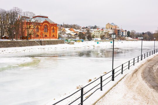 uzhgorod, ukraine - JAN 09, 2017: winter holidays in old town. embankment in snow and river uzh covered with ice. red building of old synagogue