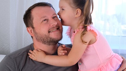 little daughter, 3 years old, tells her dad a secret, play together at home. Father's day. Handsome young man at home with his little cute girl are having fun together. Fatherhood concept, happy