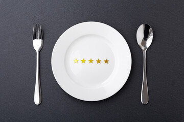 Five gold star on white plate with fork and spoon on black stone background