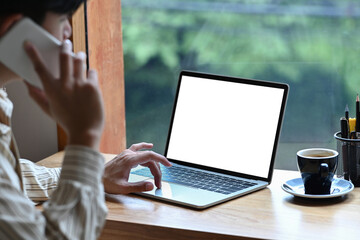 Businessman using computer laptop and talking on mobile phone while sitting in office.