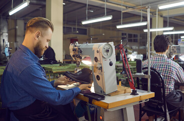 Craftsman shoe designer repairing or sewing boot on industrial stitching machine. Footwear making process. Side view shot. Handyman shoemaker working at workplace checking item on defect
