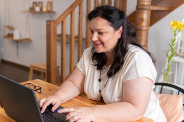 A woman is sitting in a room at a table with a laptop.