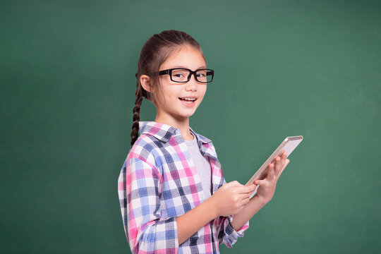 Happy student girl with glasses using tablet.Isolated on green chalkboard background.