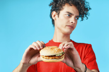 Cheerful guy with curly hair in a red t-shirt with a hamburger in his hands fast food diet