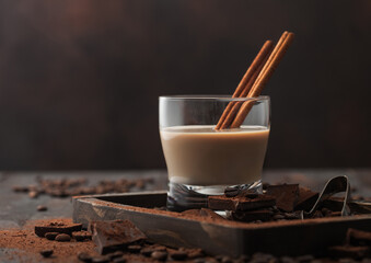 Irish cream baileys liqueur in crystal glass with cinnamon, coffee beans and powder with dark chocolate in wooden tray on dark wood background. - Powered by Adobe