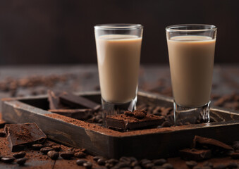 Irish cream baileys liqueur in shot glasses in wooden tray with coffee beans and powder on dark wood background.