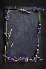 Top view of a black slate board with bunch of lavender flowers around as a frame on a dark background. Romantic theme with copyspace for your text.