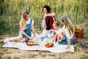 Three generations of women of the same family on a picnic, a grandmother pours tea from a thermos to her daughters and granddaughter