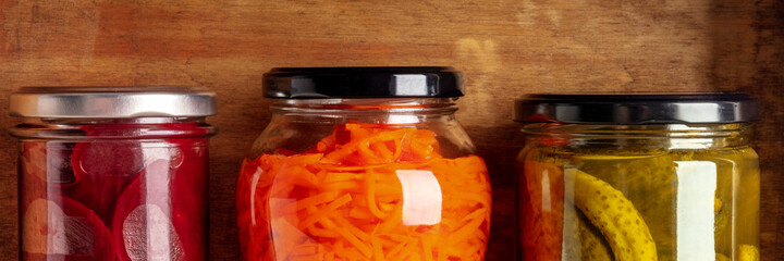 Pantry preserves panorama. Pickled carrot, beetroot, and gherkins in glass jars on a wooden shelf in a kitchen cellar