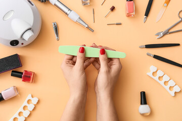 Female hands with nail file and tools for manicure on color background