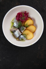 Fish herring with potatoes traditional Russian Swedish Atlantic dish salted fish with baked potato slices in a white plate On a black background large top view with space for text