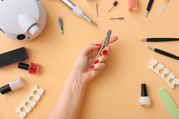 Female hand with scissors and tools for manicure on color background