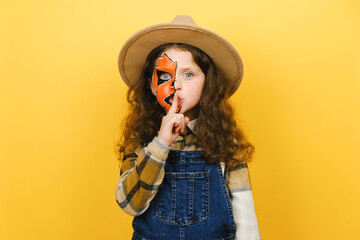 Secret charming fun curly little girl child with Halloween makeup mask wears brown hat, say hush be...