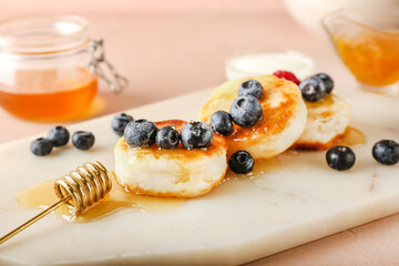 Board with tasty cottage cheese pancakes, berries and honey on table, closeup