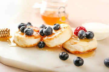 Board with tasty cottage cheese pancakes, berries and honey on table, closeup