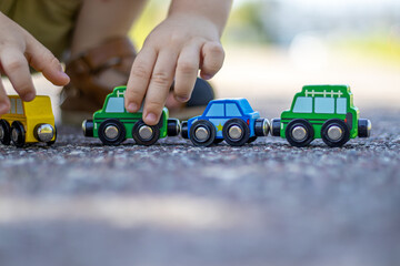 A kid is playing with a train made from wood, with magnet connections are on the asphalt, outside. Concept: playing outdoor, summertime, eco toys.