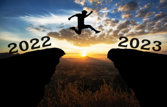 A young man jump between 2022 and 2023 years over the sun and through on the gap of hill  silhouette evening colorful sky. happy new year 2022.