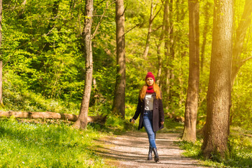 Obraz premium Latin girl with a black jacket, scarf and red woolen hat enjoying in an autumn park, walking along a path