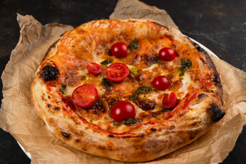 Delicious pizza with tomatoes pepperoni Margarita fresh Pastries on a black concrete background. Top view of a hot pepperoni pizza. With space for text. He was lying flat. Ruddy dough on kraft paper 