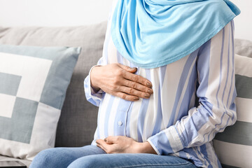 Pregnant Muslim woman sitting on sofa at home